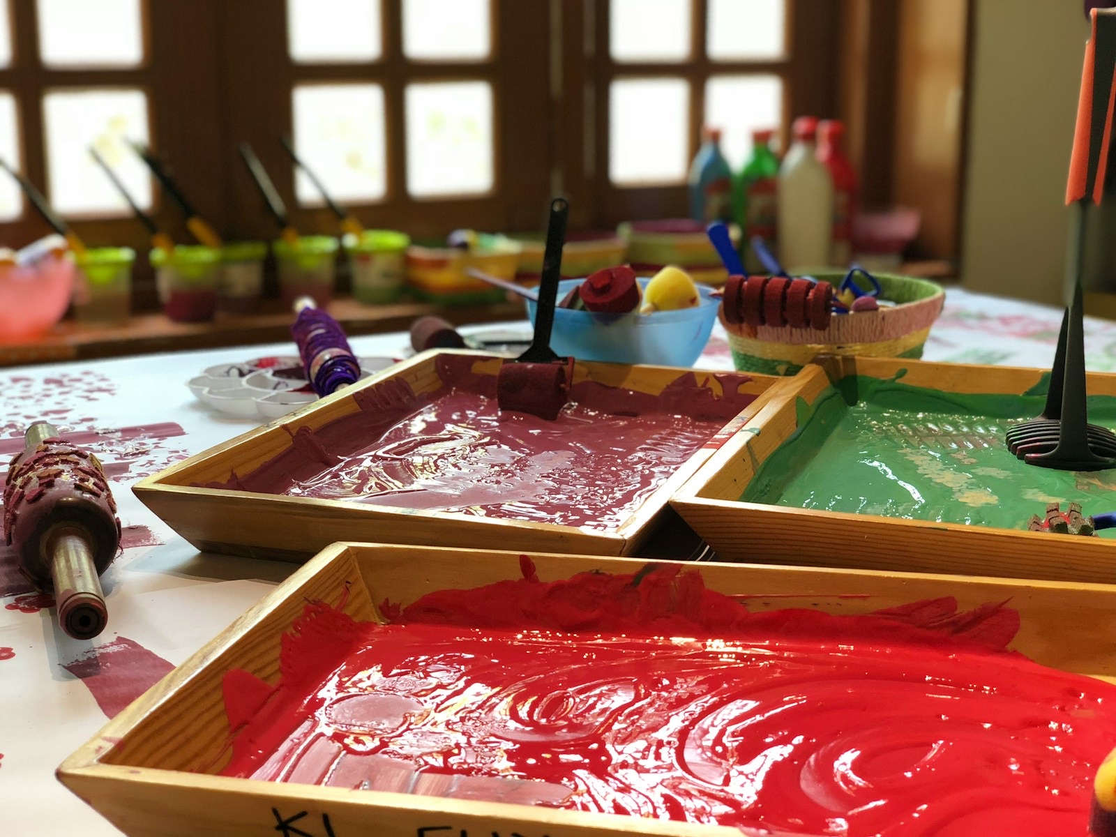 Trays of red and green paint with rollers on a low table